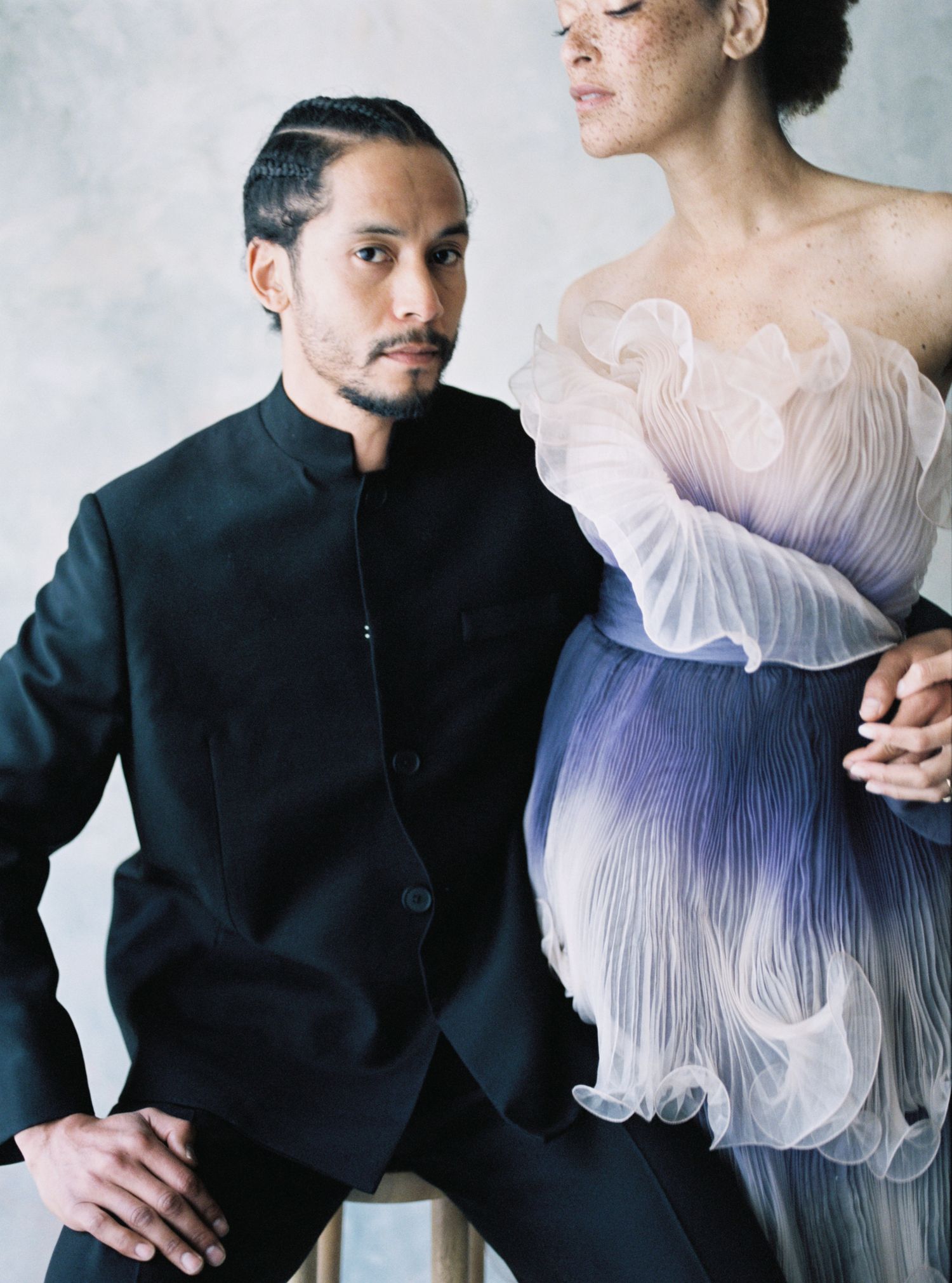Elegant couple posing together, man in black mandarin collar suit, woman in sculptural ombre ruffle gown.