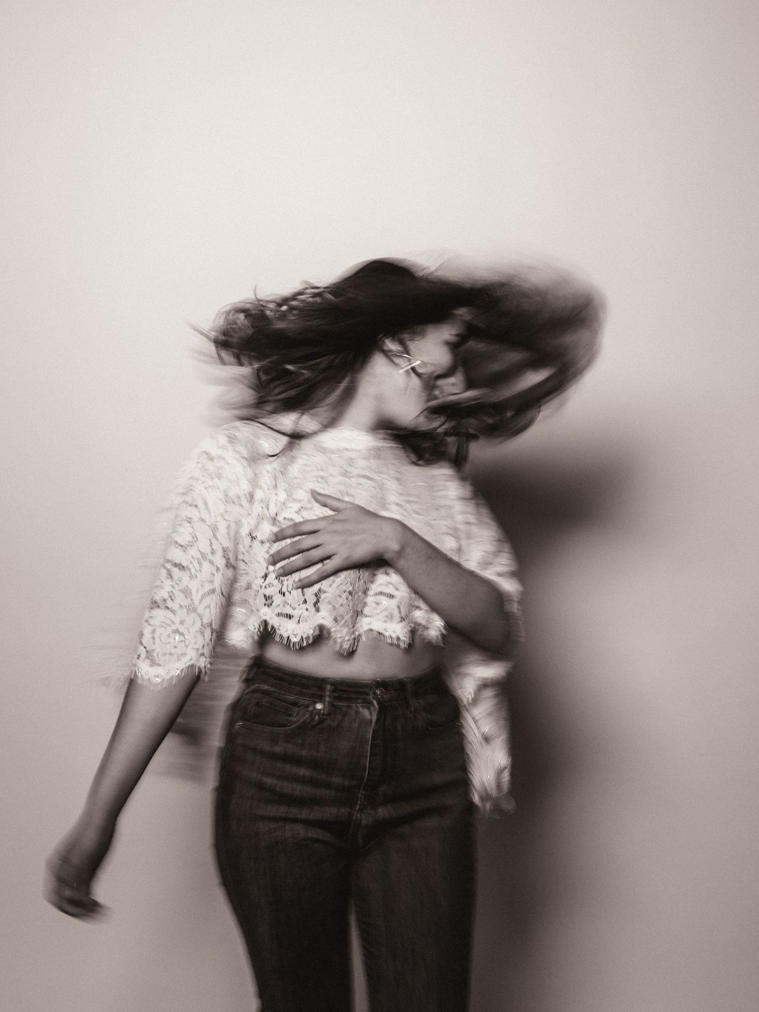 Black and white photo of a woman in lace crop top and jeans with hair flying, captured in motion blur.