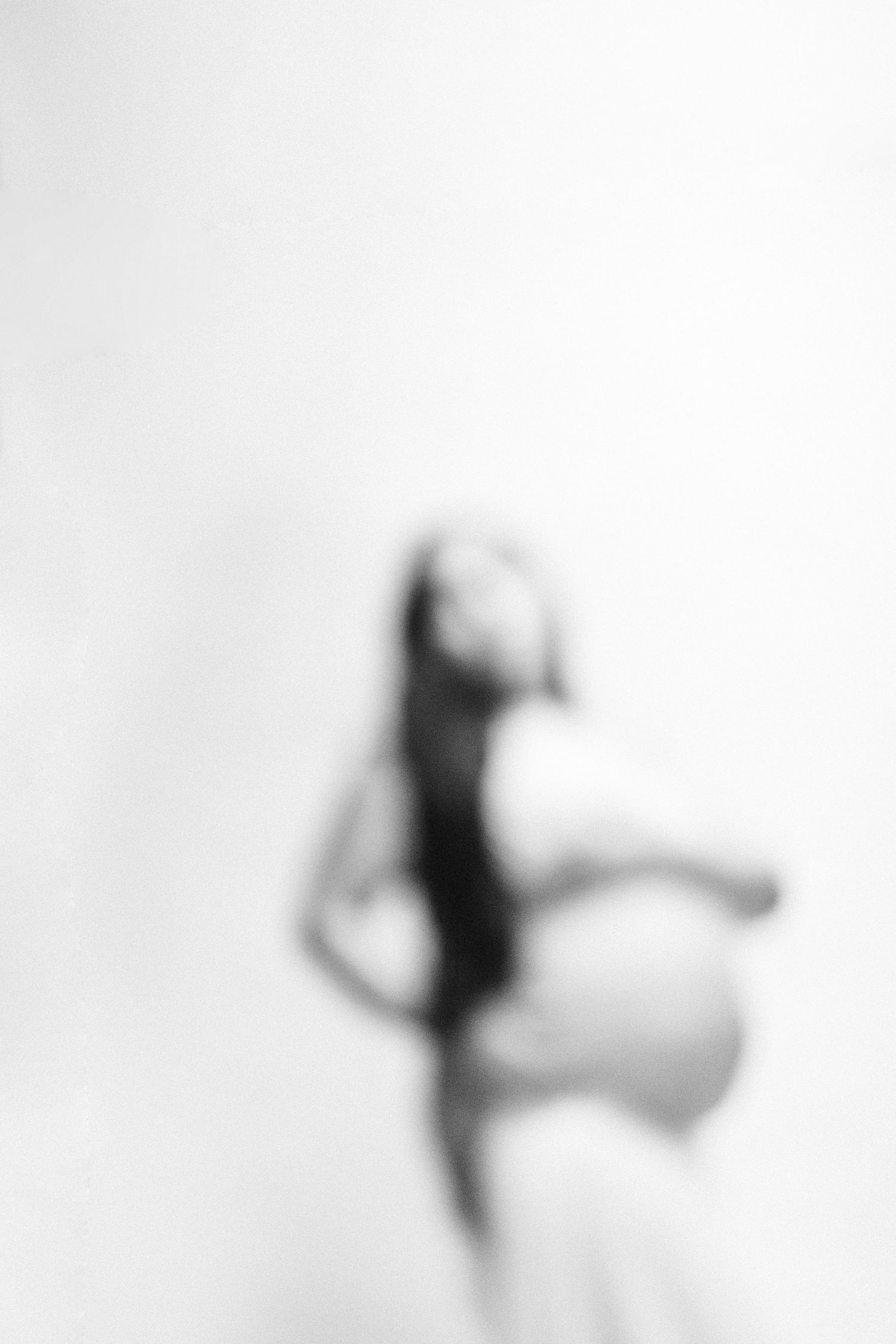 Blurred black and white artistic maternity photo of a pregnant woman in profile against white background.