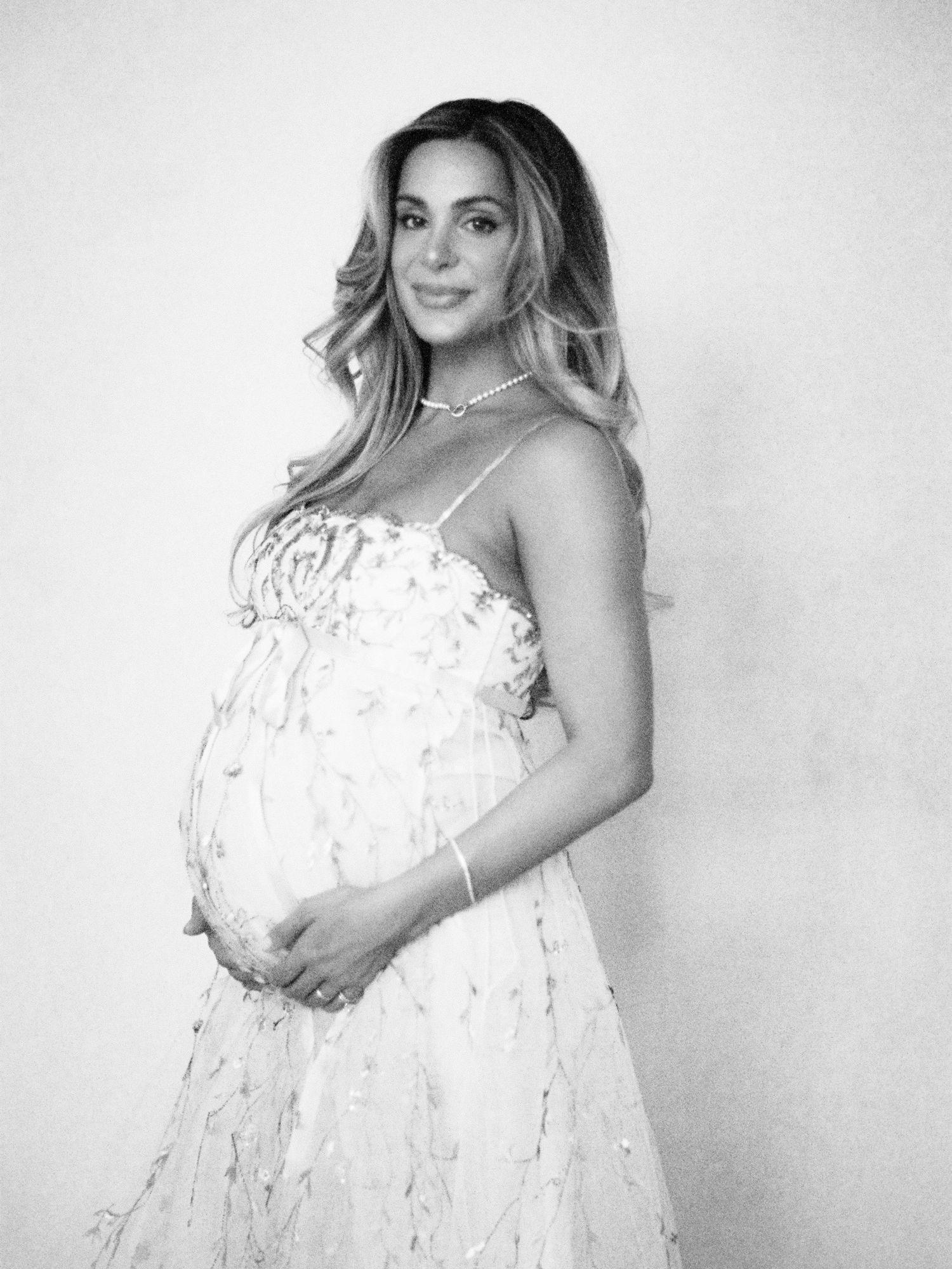 Pregnant woman in white floral dress cradling baby bump, elegant philly maternity portrait in black and white.