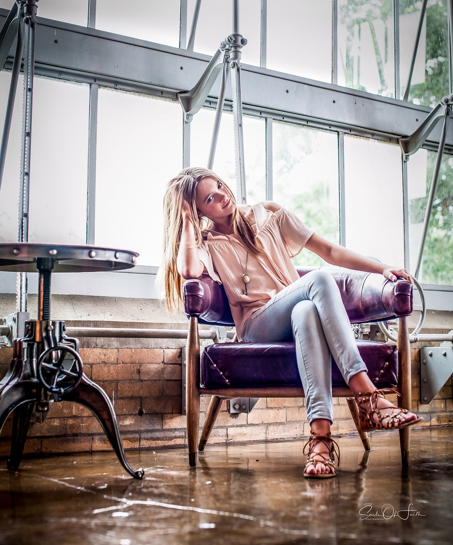 Smiling blonde woman relaxing in a purple leather chair in a bright industrial loft with large windows.