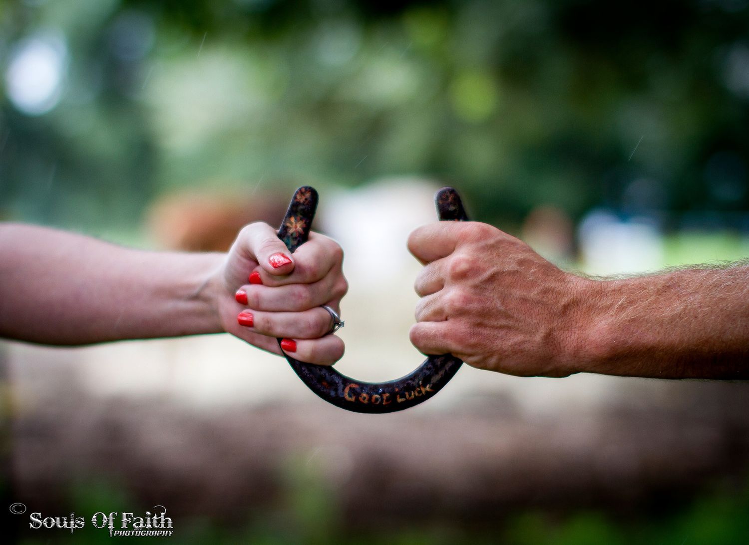 Two hands grip a decorative horseshoe together outdoors, one with red nails, symbolizing partnership and faith.