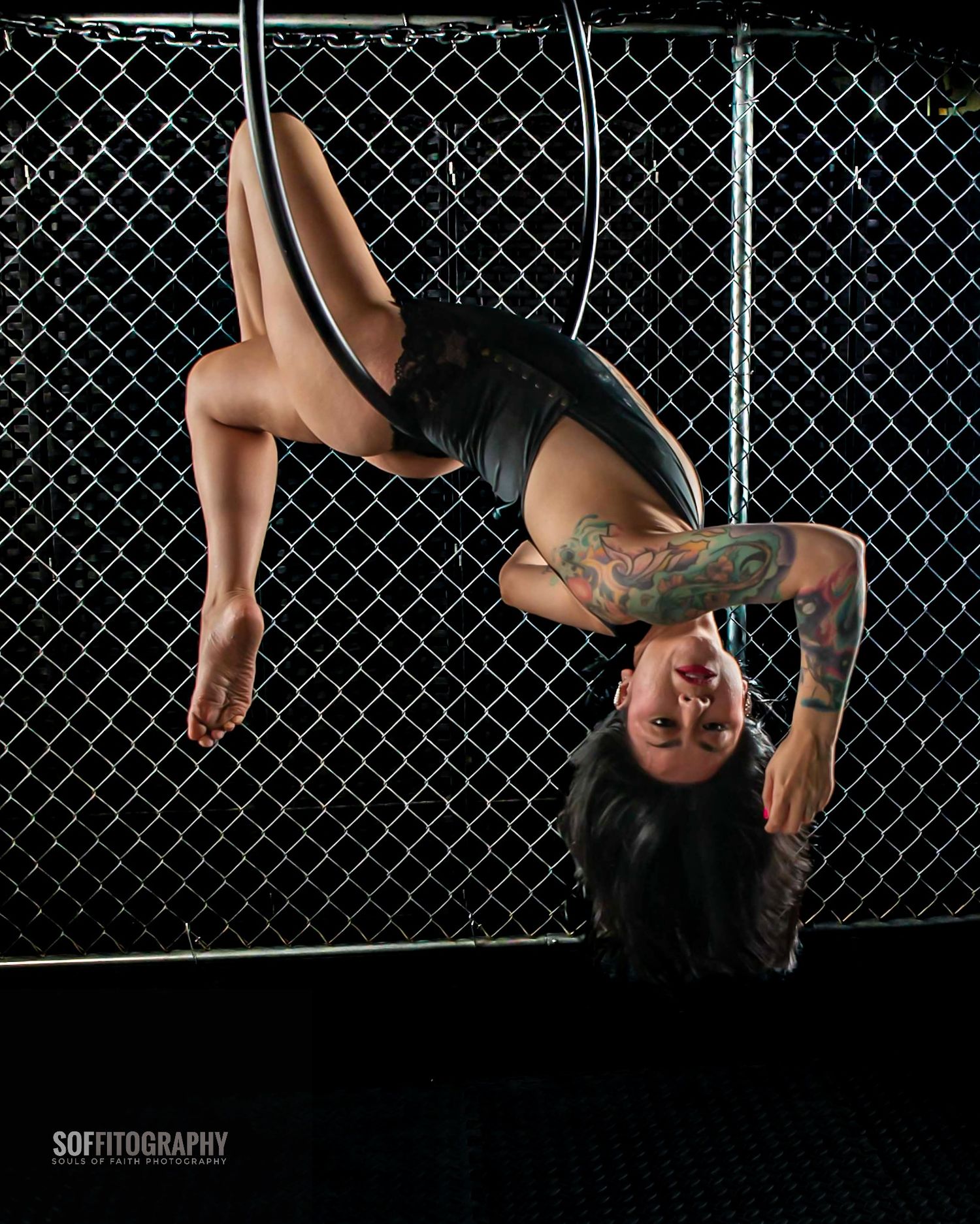 Tattooed woman performing aerial pole dance upside down in front of chain-link fence, photographed by Soffitography.