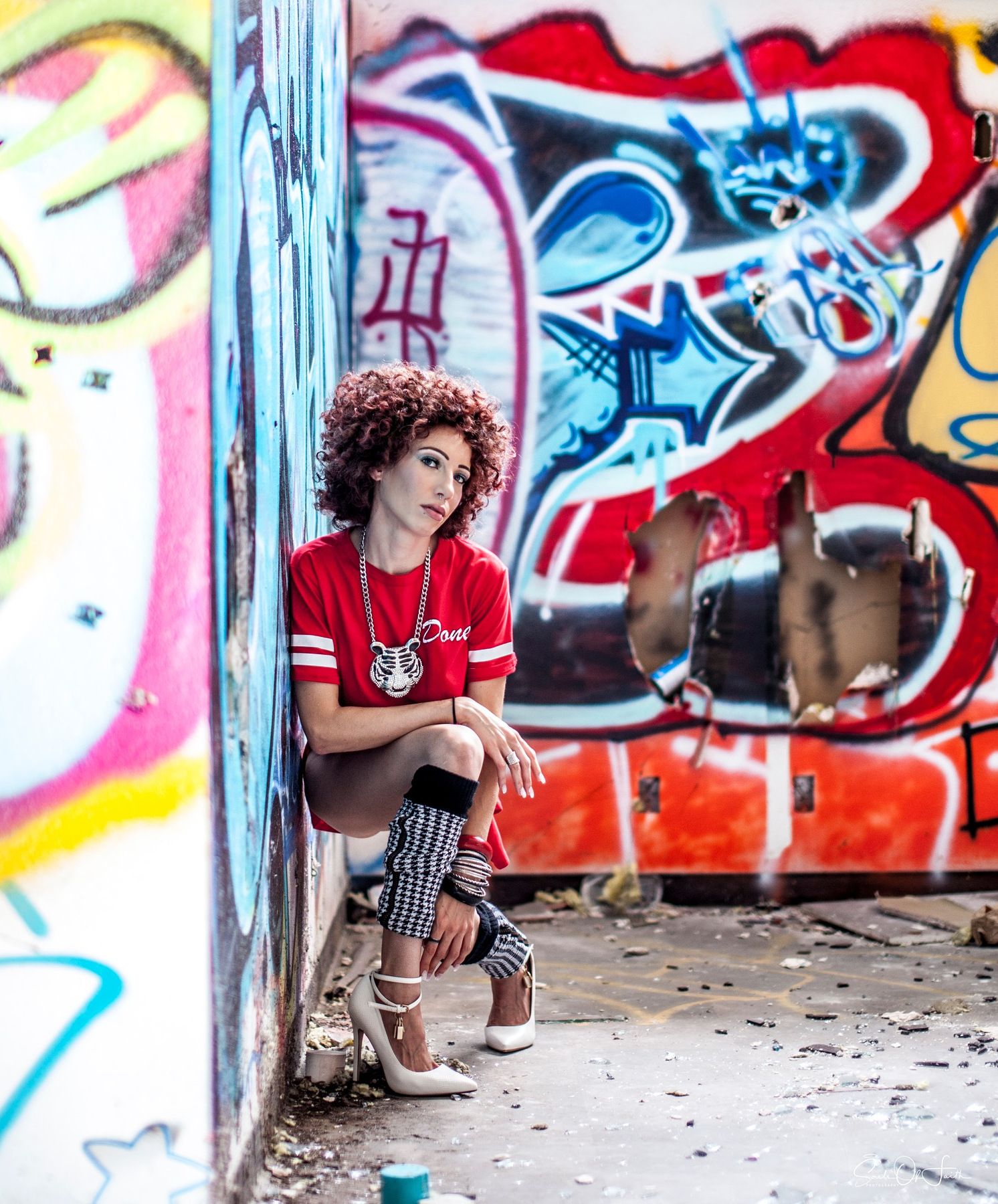 Young woman with curly hair in red shirt sits against colorful graffiti wall in urban setting. urban gothic emo fun abandoned sylized