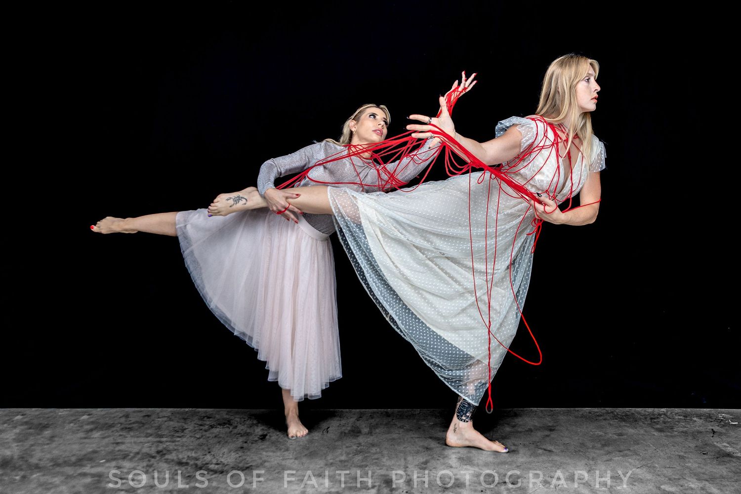 Two ballet dancers in flowing gray dresses perform with red ribbons against a dark background.