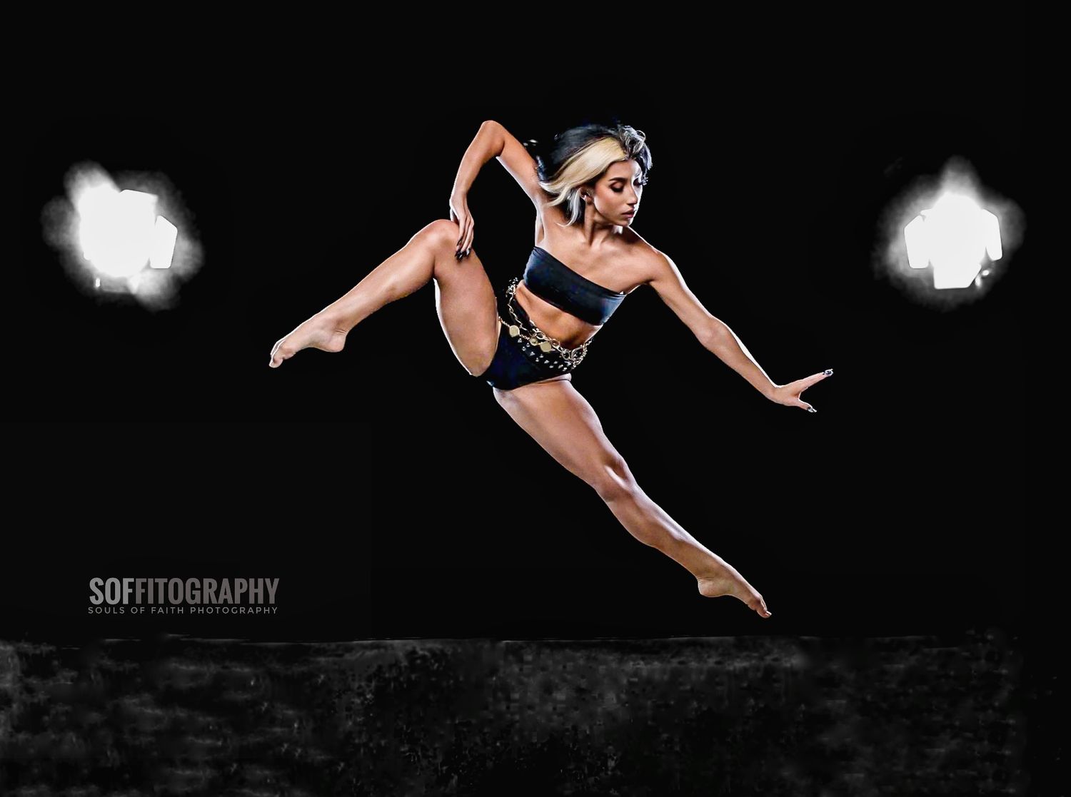 A female dancer leaps gracefully against a dark background, showcasing athletic form in a black crop top and shorts.