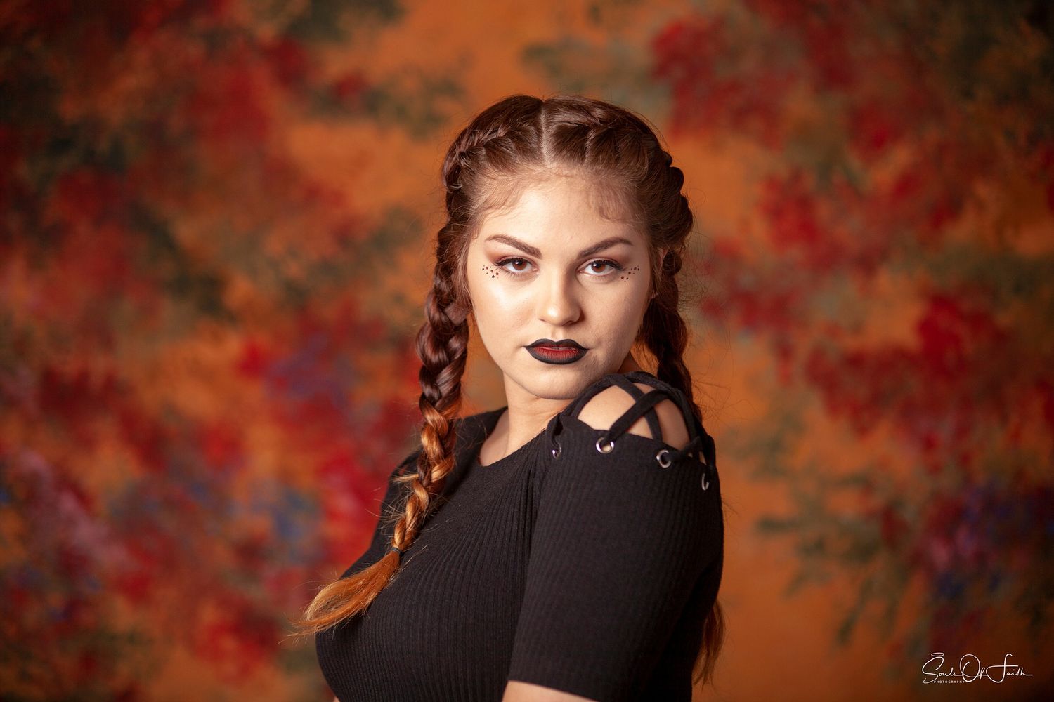 Young woman with braided hair in black top poses against vibrant floral backdrop.