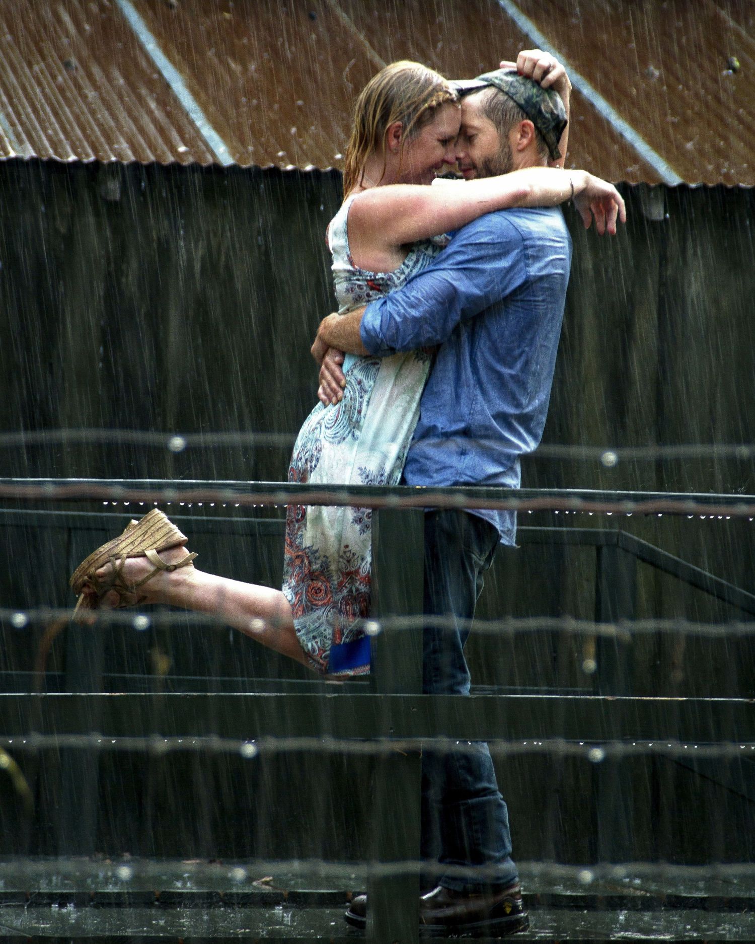 Romantic couple embracing and kissing in the rain on a balcony, sharing a passionate moment outdoors.