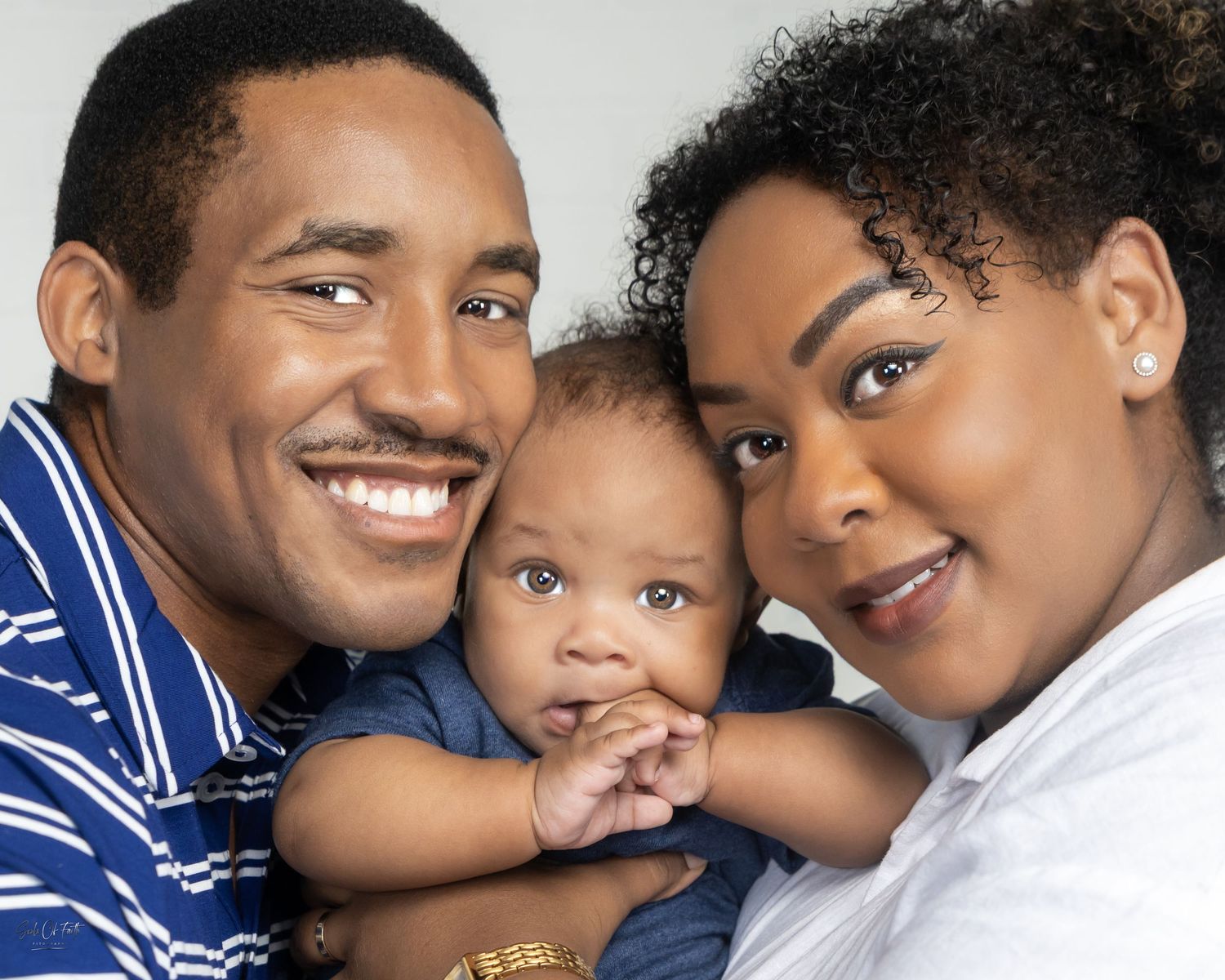 Happy family portrait of smiling parents with their adorable baby, posing together against a light background.
