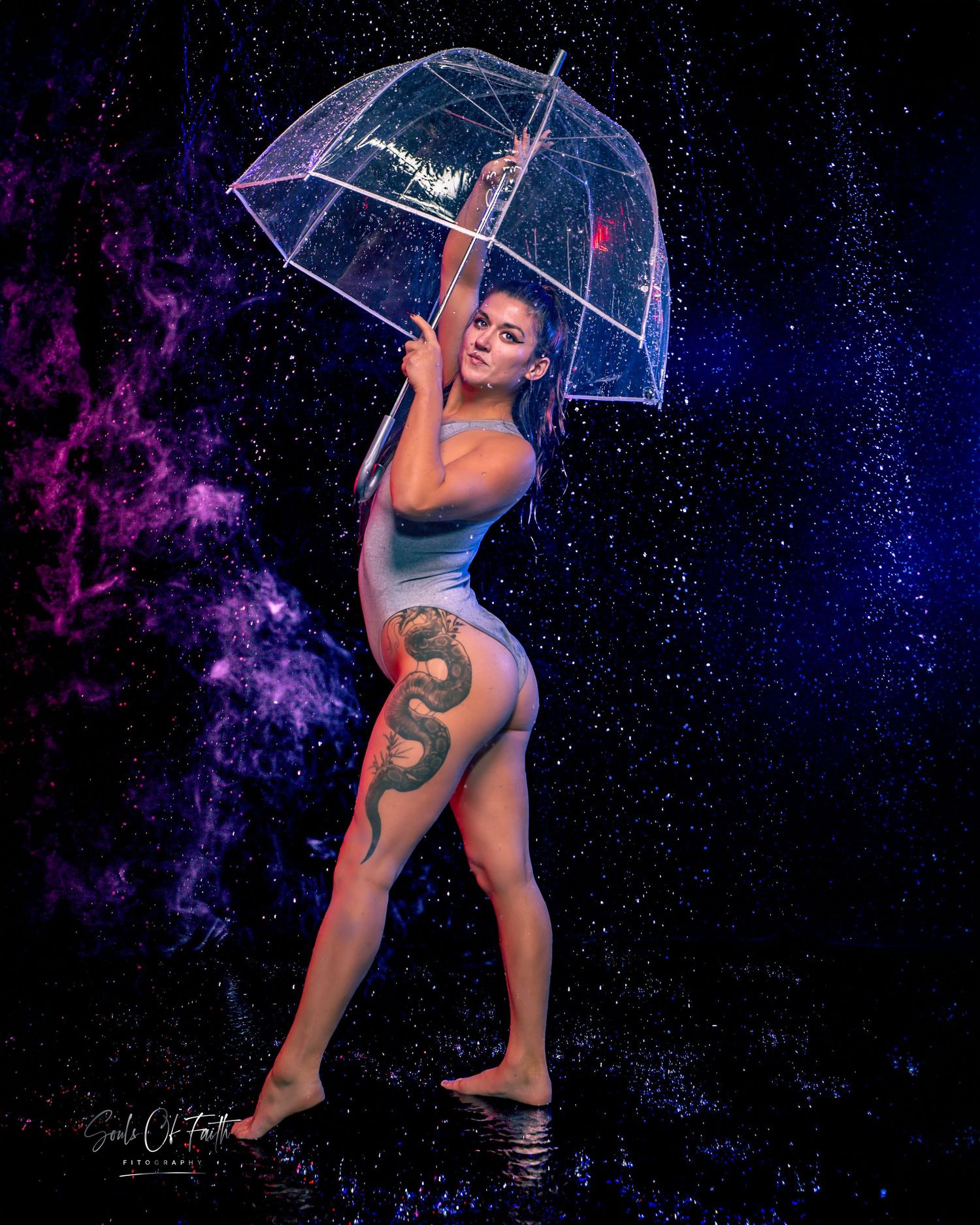 Woman with snake tattoo poses in swimsuit holding clear umbrella under sparkling cosmic rain backdrop.