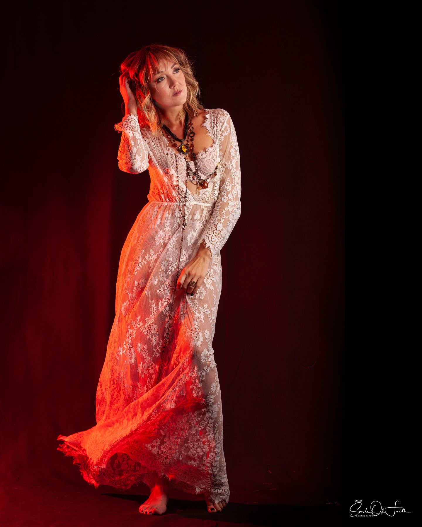 Woman in white lace gown posed dramatically under red lighting against dark background.