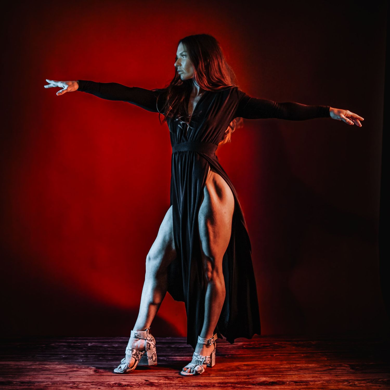 Woman in black dress dancing with arms outstretched against a dramatic red background.