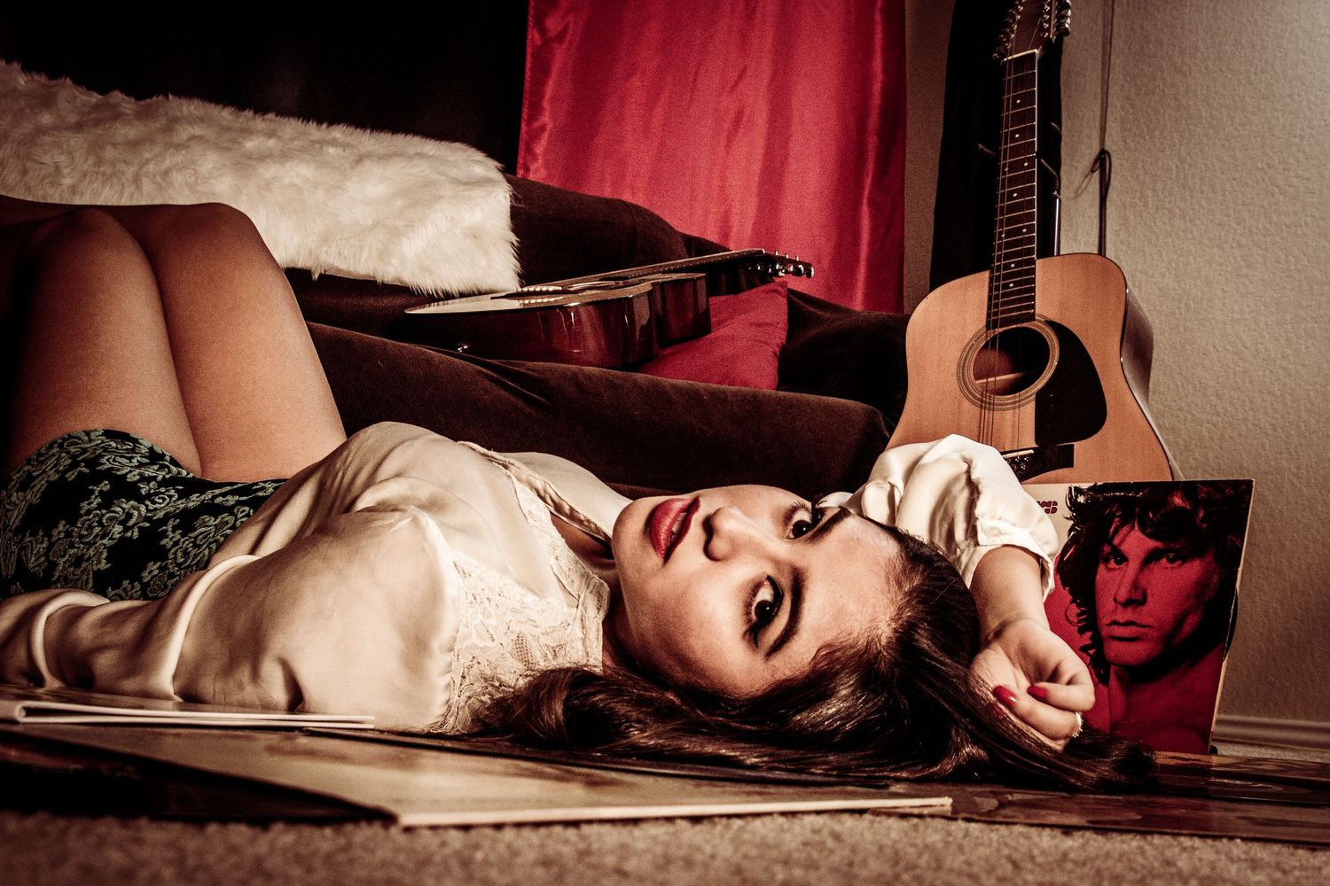 Young woman lying on floor beside acoustic guitar and The Doors album cover in moody room.