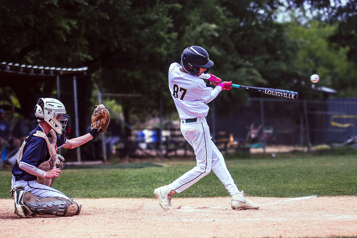 Baseball batter in jersey #87 swings at a pitch during a sunny outdoor game, with catcher crouching behind home plate.
