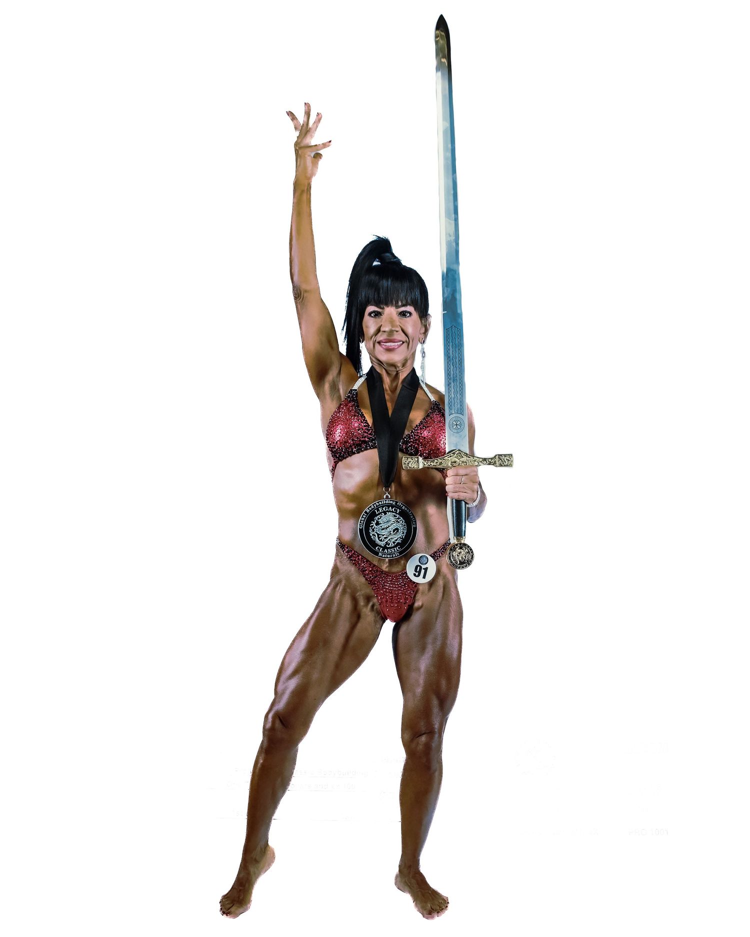 Muscular female bodybuilder in red bikini costume poses dynamically holding a long sword with one arm raised.