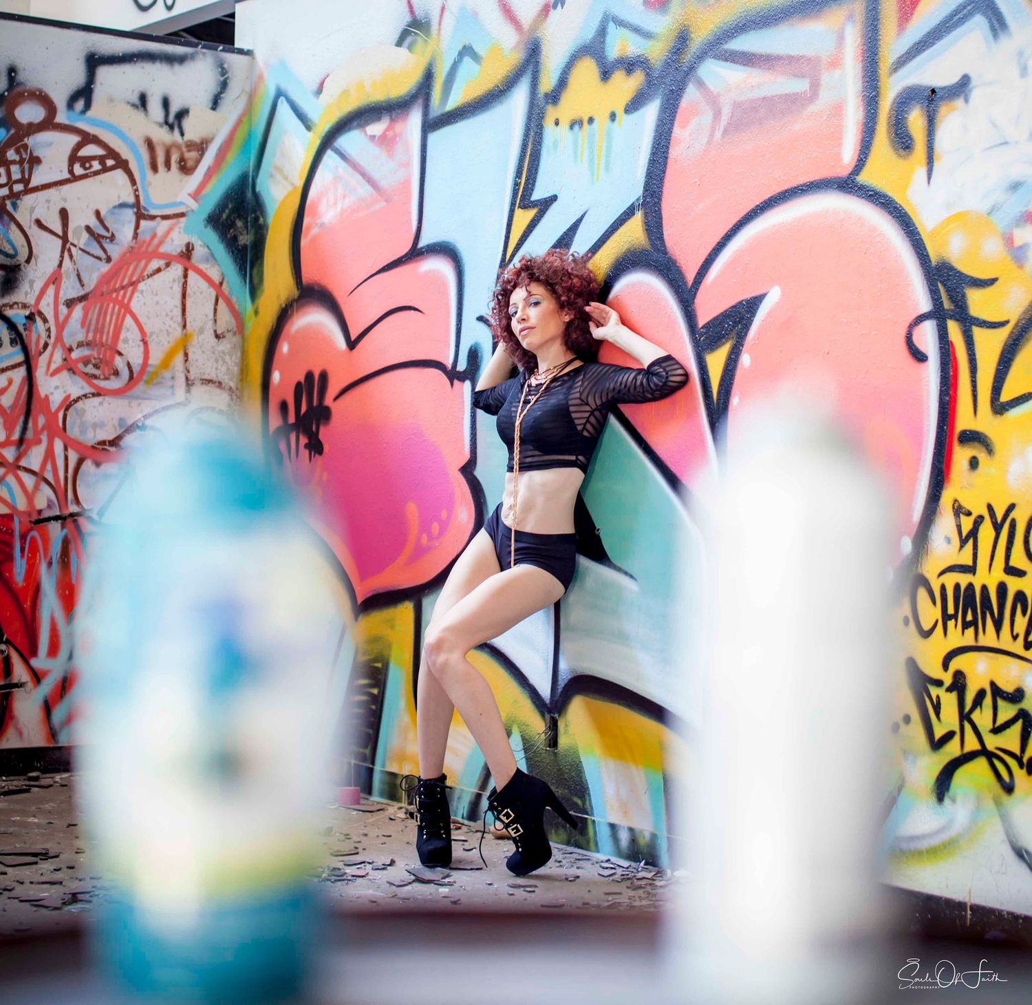 Young woman in crop top and shorts posing confidently against a vibrant colorful graffiti wall outdoors.