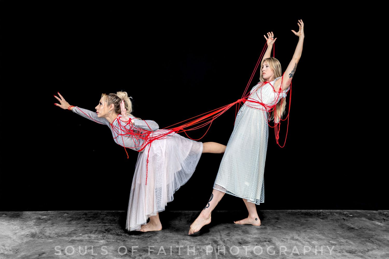 Two ballet dancers in white dresses perform with red ribbons against a dark background.