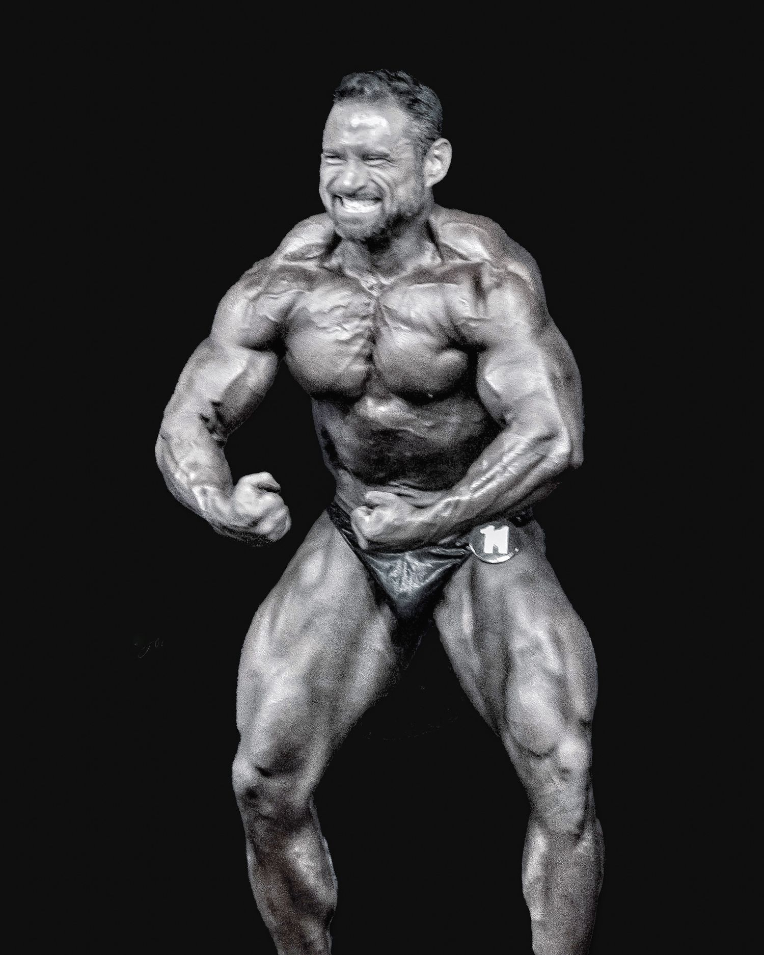 Black and white photo of a muscular male bodybuilder flexing on stage during a competition.