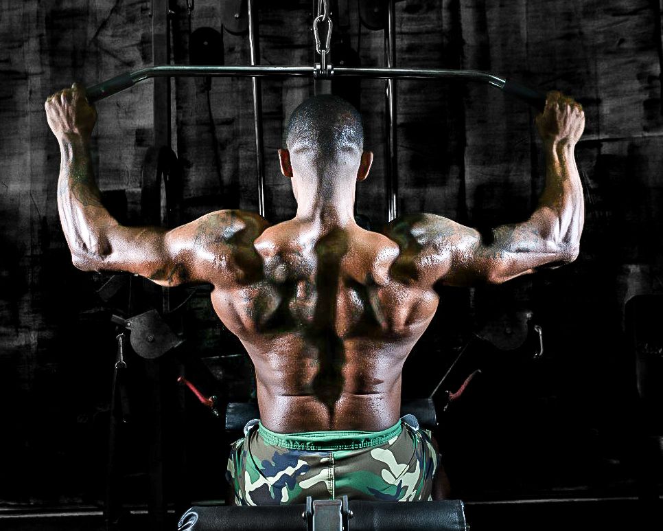 Muscular bodybuilder performing lat pulldown exercise showing defined back muscles in a gym setting.