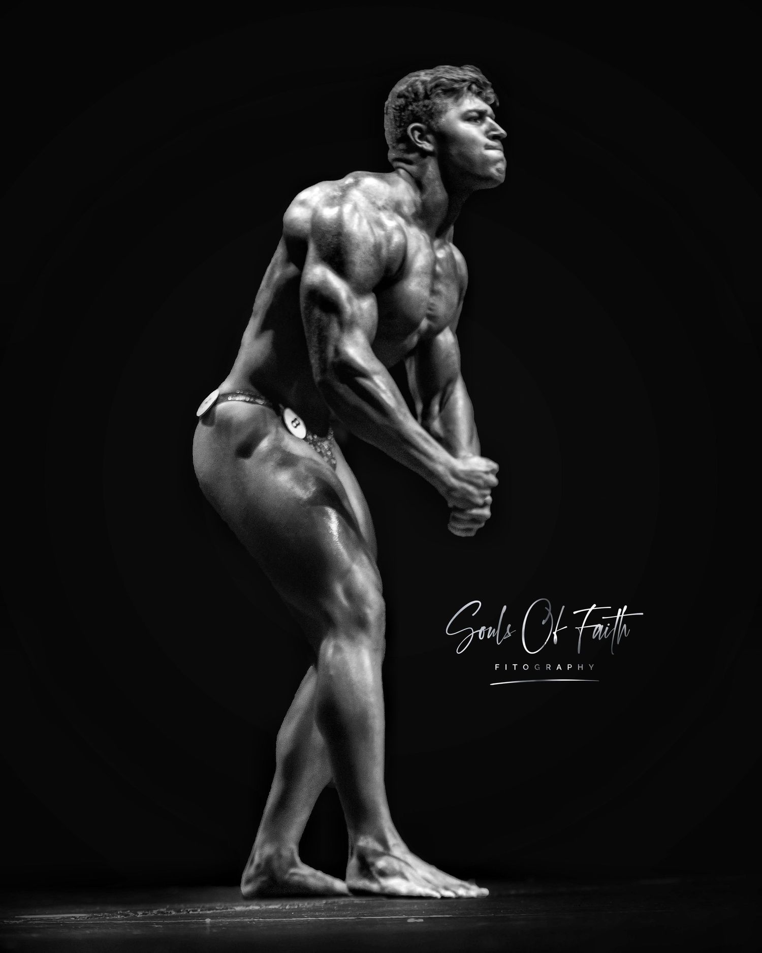 Black and white photo of a muscular male bodybuilder posing on stage, showcasing defined muscles in competition.