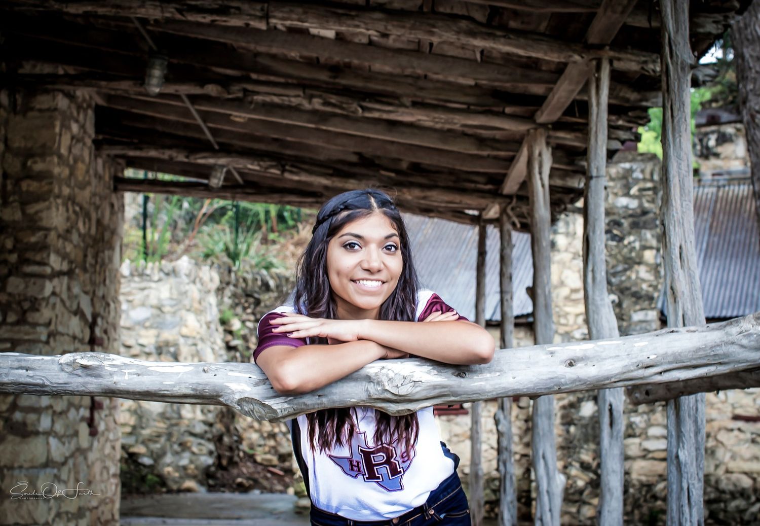 Young woman smiling and leaning on a rustic wooden fence in a rural village setting.