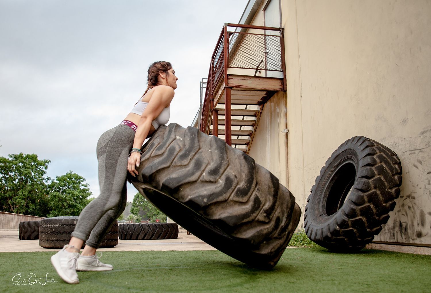 Woman in athletic wear flipping a large tractor tire outdoors during a CrossFit workout session.