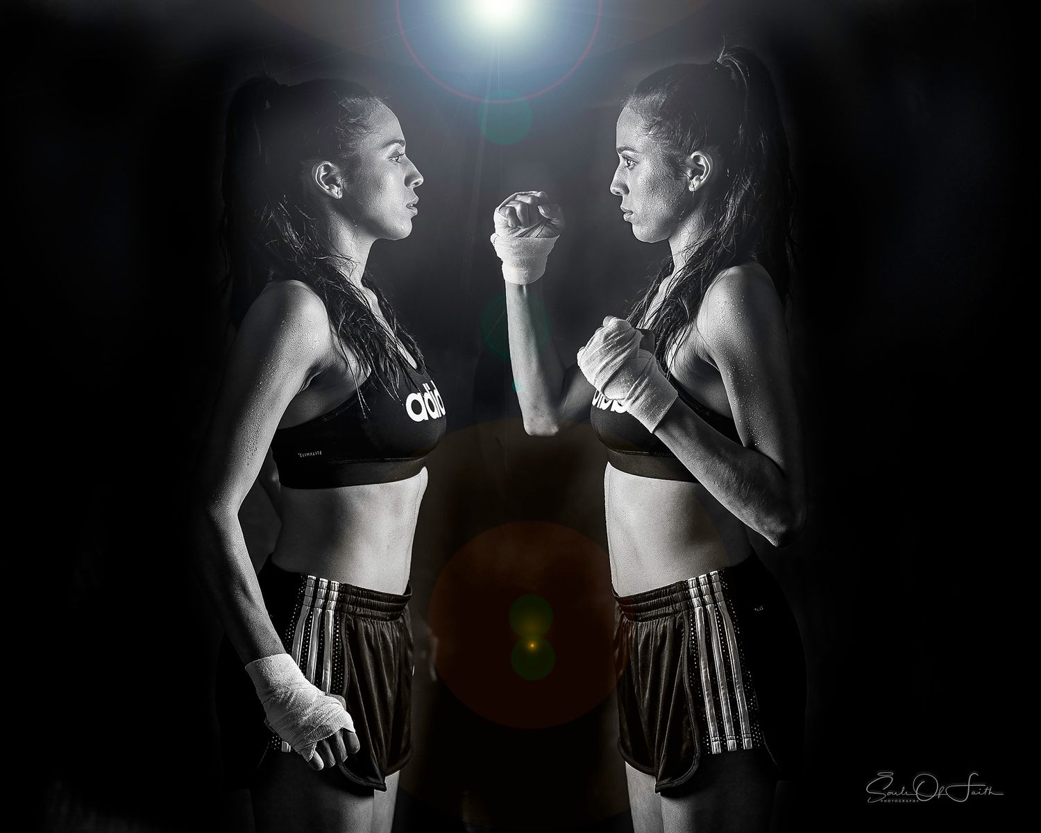 Two female boxers in Adidas gear face off in a dramatic black and white mirrored pose under a spotlight.