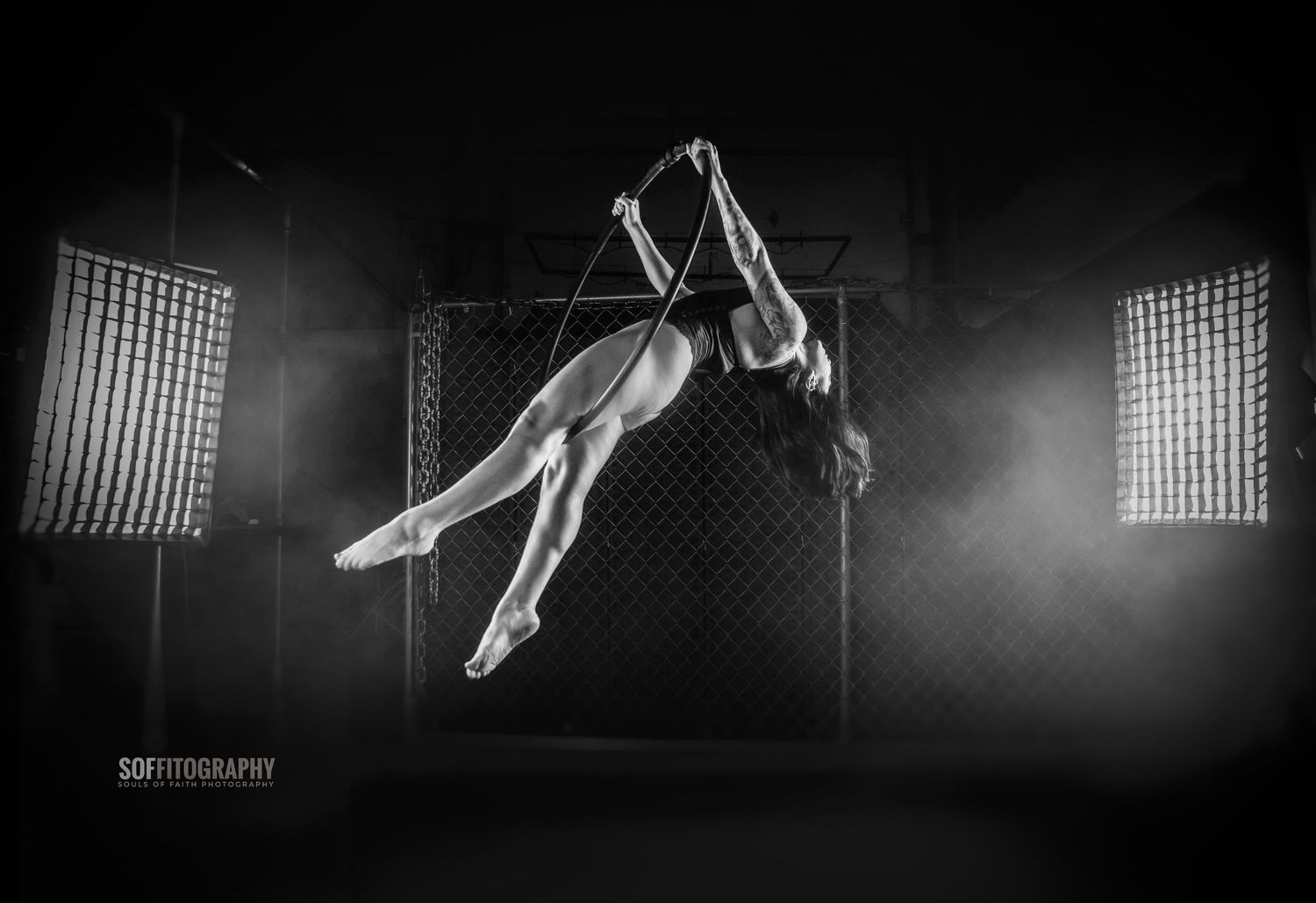 Black and white photo of an aerial acrobat performing a dramatic pose suspended mid-air in a dark studio.
