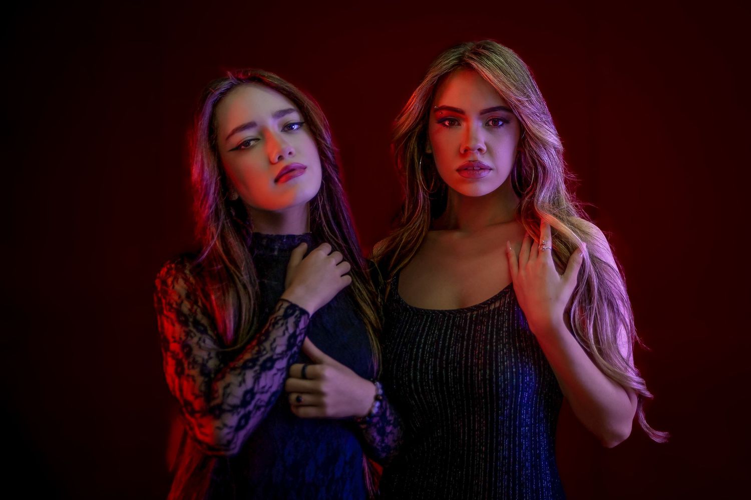 Two young women posing dramatically under red and purple studio lighting against a dark background.