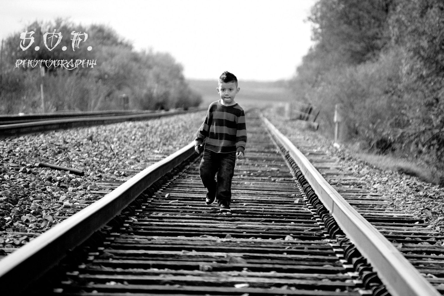 Black and white photo of a young boy walking alone on railroad tracks in a rural setting.
