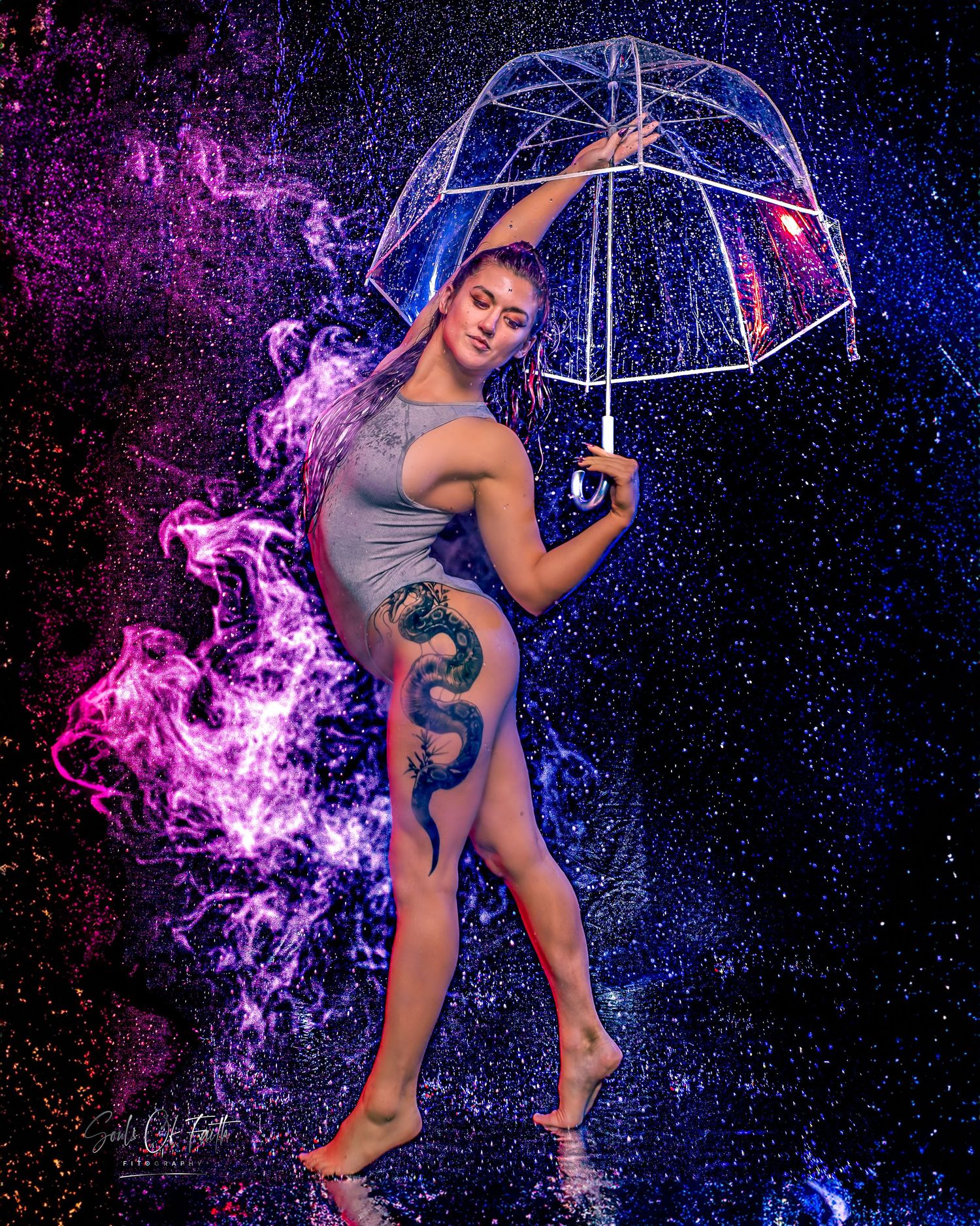 Woman with dragon tattoo poses under clear umbrella amid colorful blue and purple smoke and water droplets.