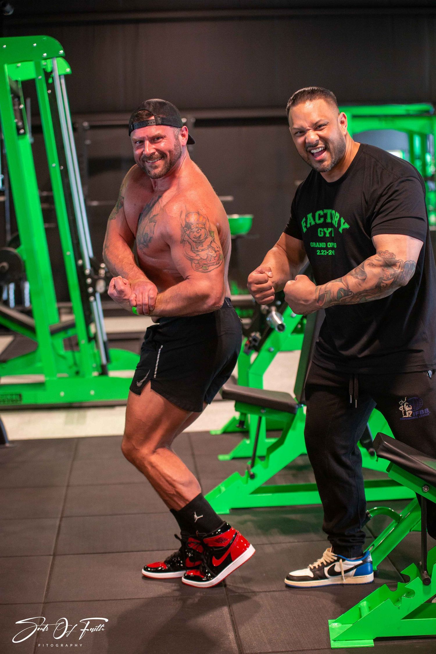 Two muscular men flexing and smiling in a modern gym with bright green equipment.