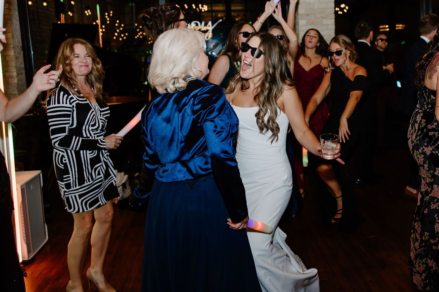 Lively reception dance party with guests in formal attire under dim lighting.