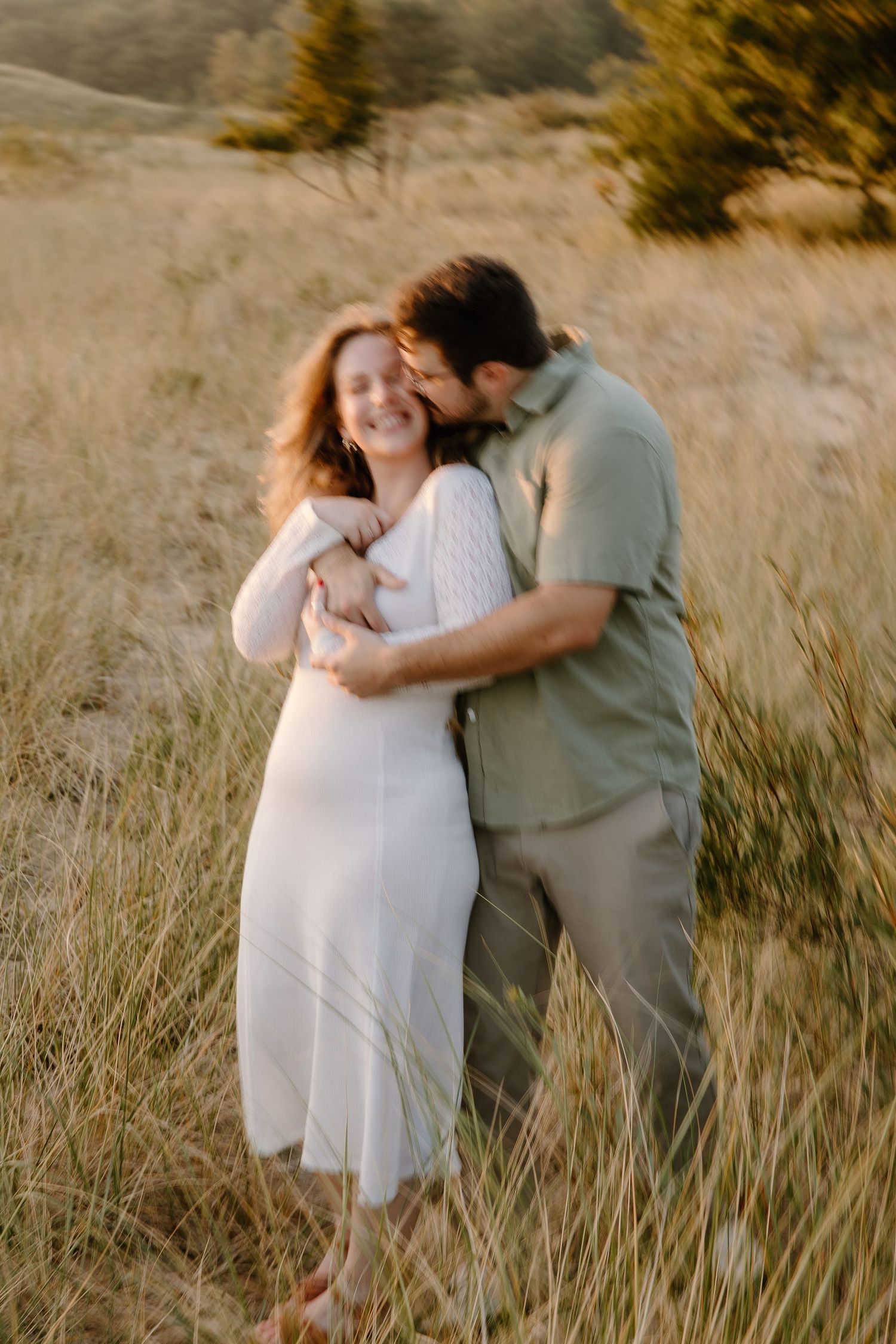 A maternity photoshoot in a sun-kissed field features a couple sharing intimate moments.