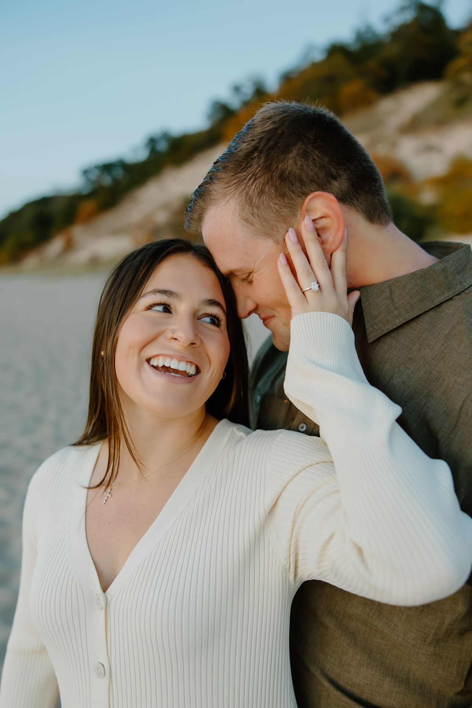 Romantic couple in white and brown sweaters sharing tender moment on beach.