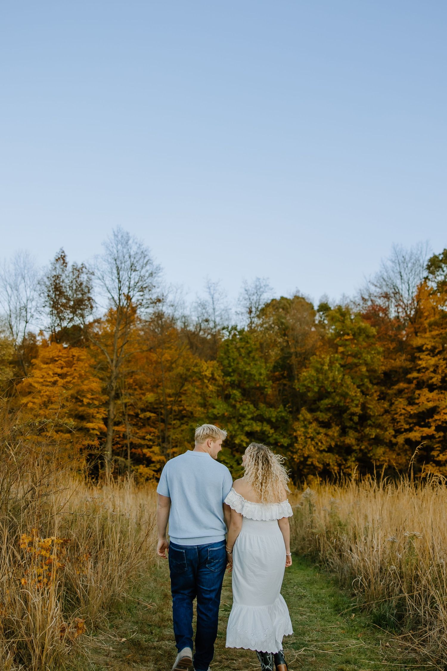 Couple walking along path through golden prairie grass at sunset.