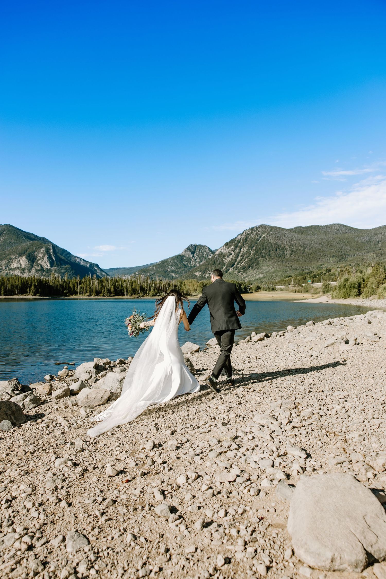 Rocky beach landscape with mountains and lake against vibrant blue sky.