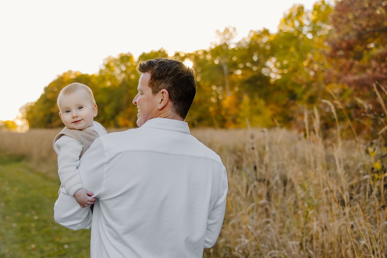 An adult holds a small child while standing in a field during sunset.
