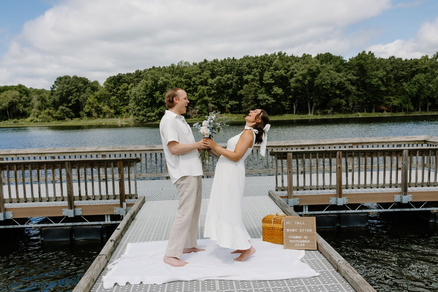 A couple shares a playful moment during their wedding ceremony on a dock overlooking a serene lake.