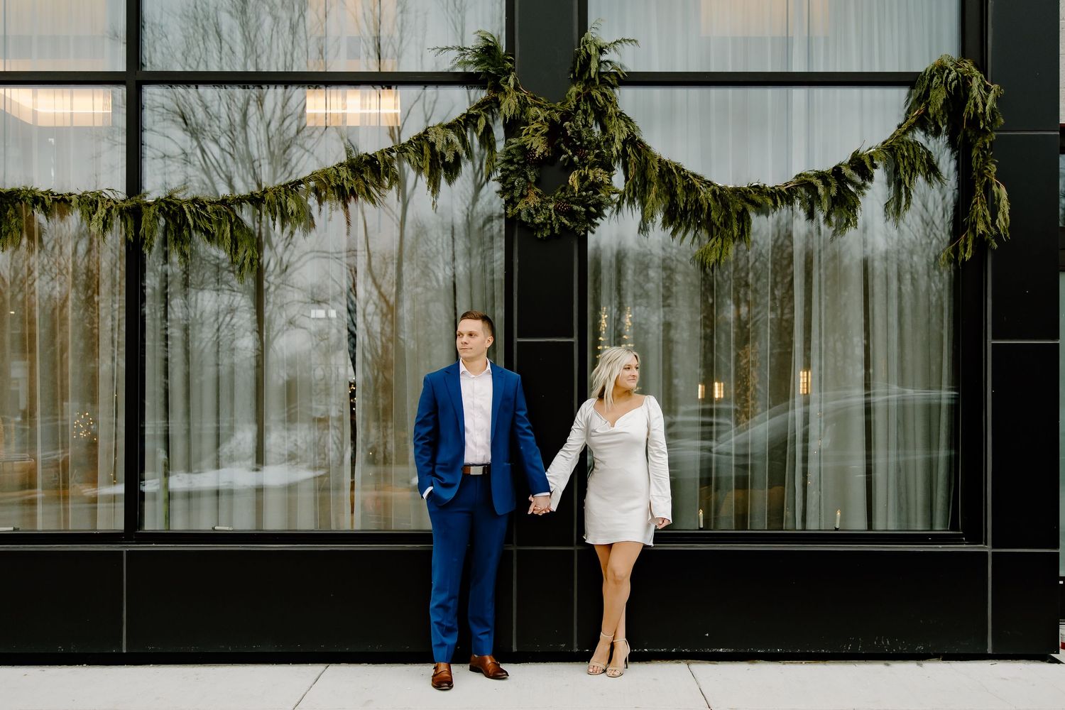 Couple walking outside modern glass building with winter trees in background.