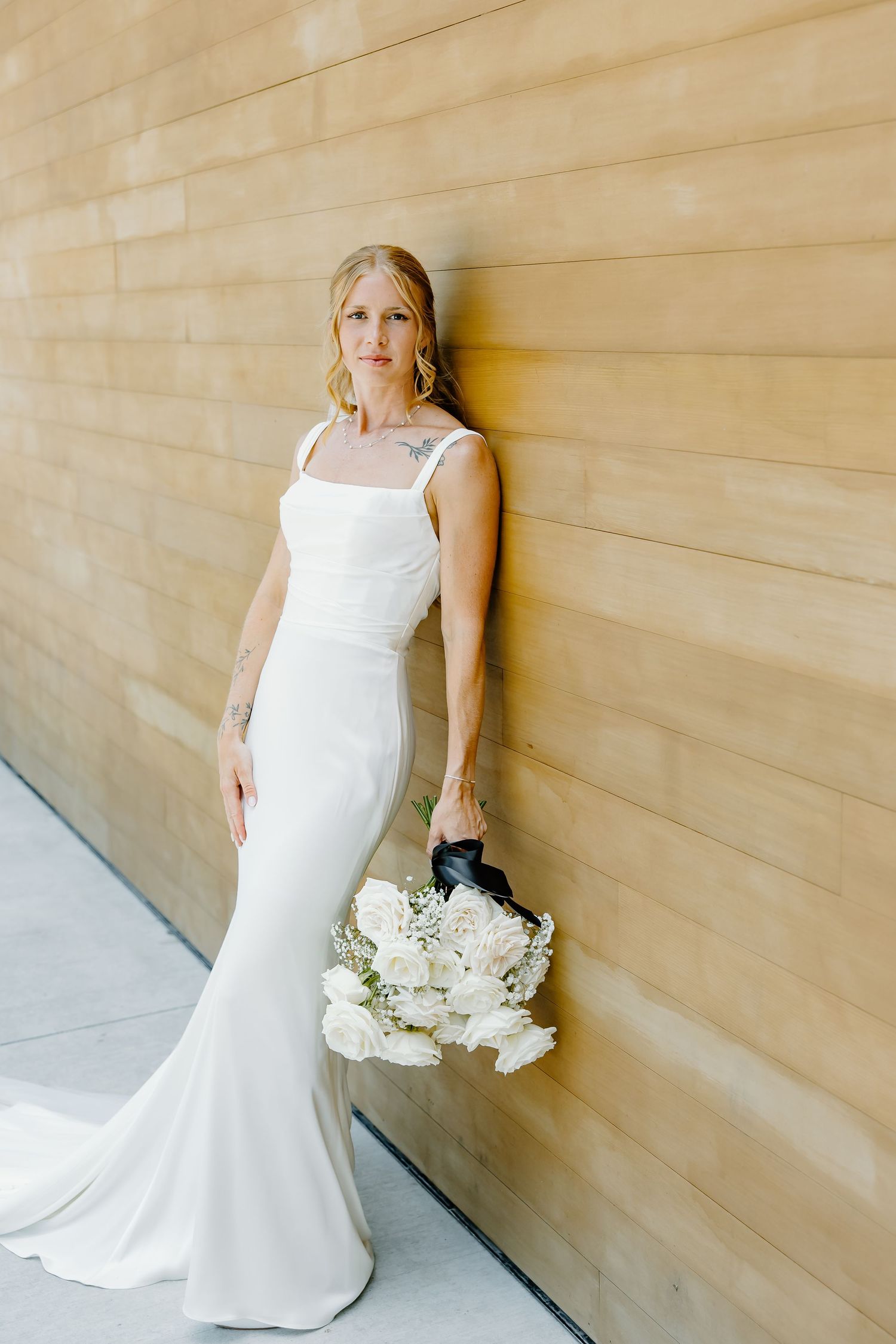 Elegant bridal portrait against a wooden wall showcasing a fitted white wedding gown and bouquet.