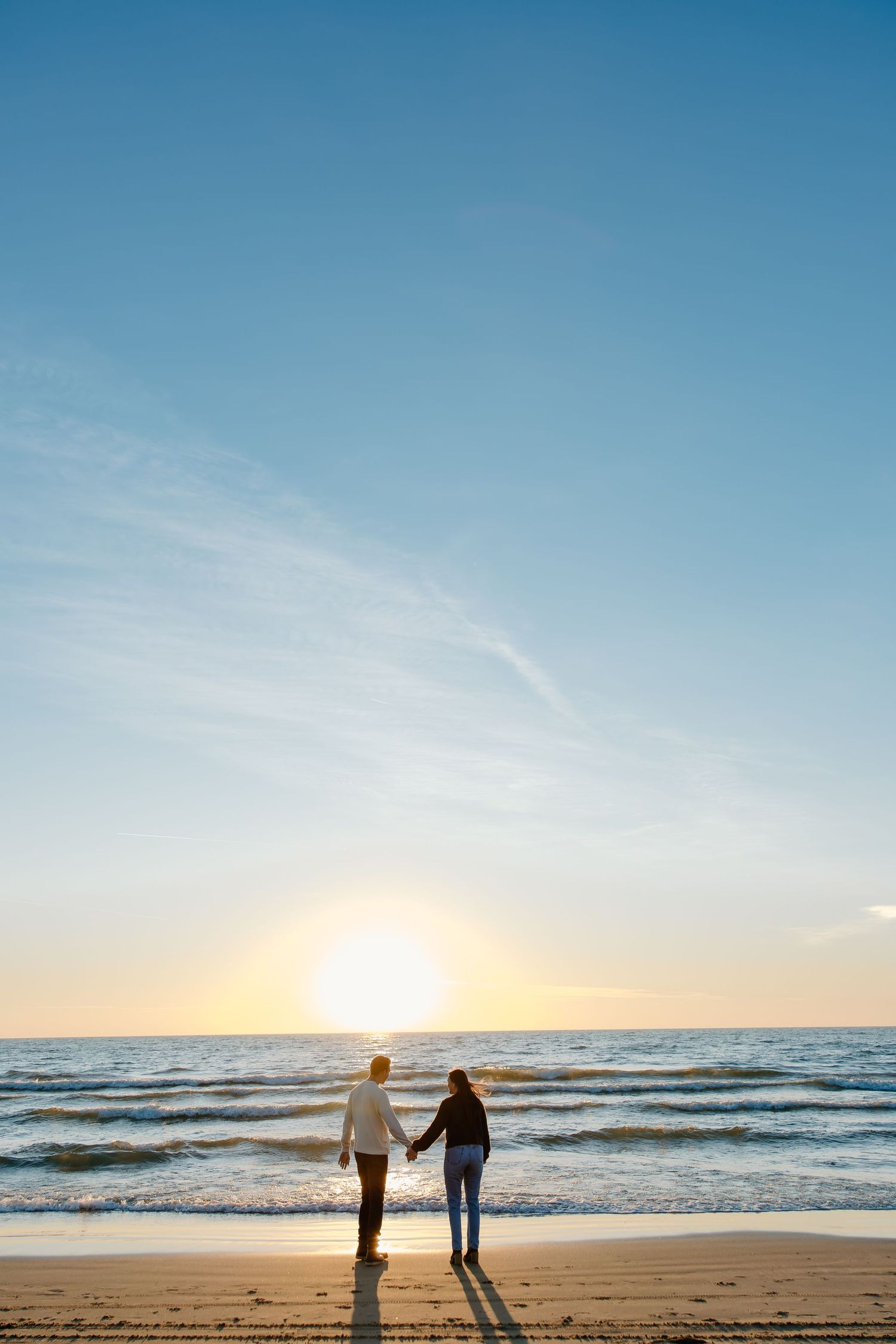 Two figures walking hand in hand along a serene beach during sunset.