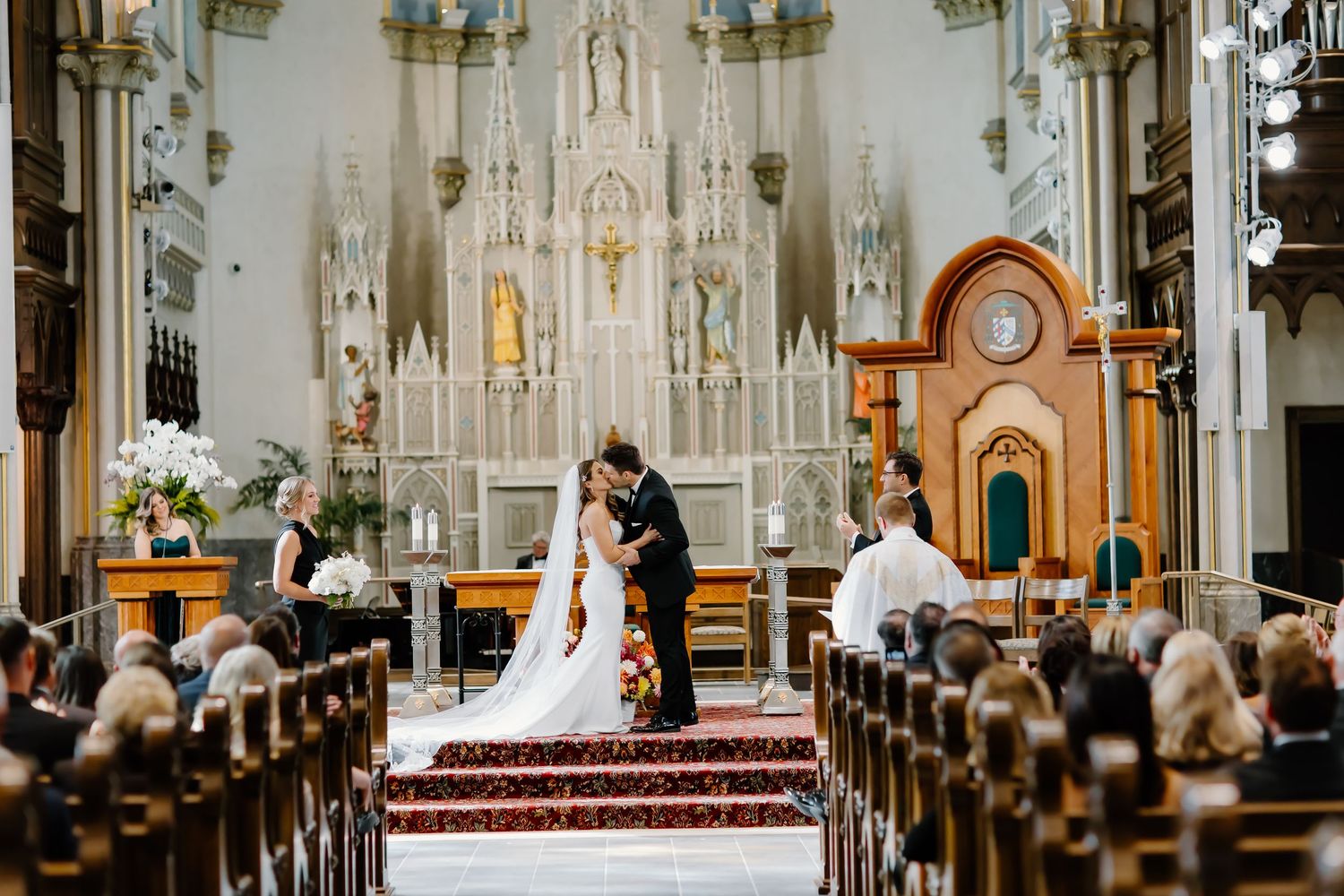 Wedding ceremony in progress inside a majestic cathedral with wooden pews and soaring architecture.