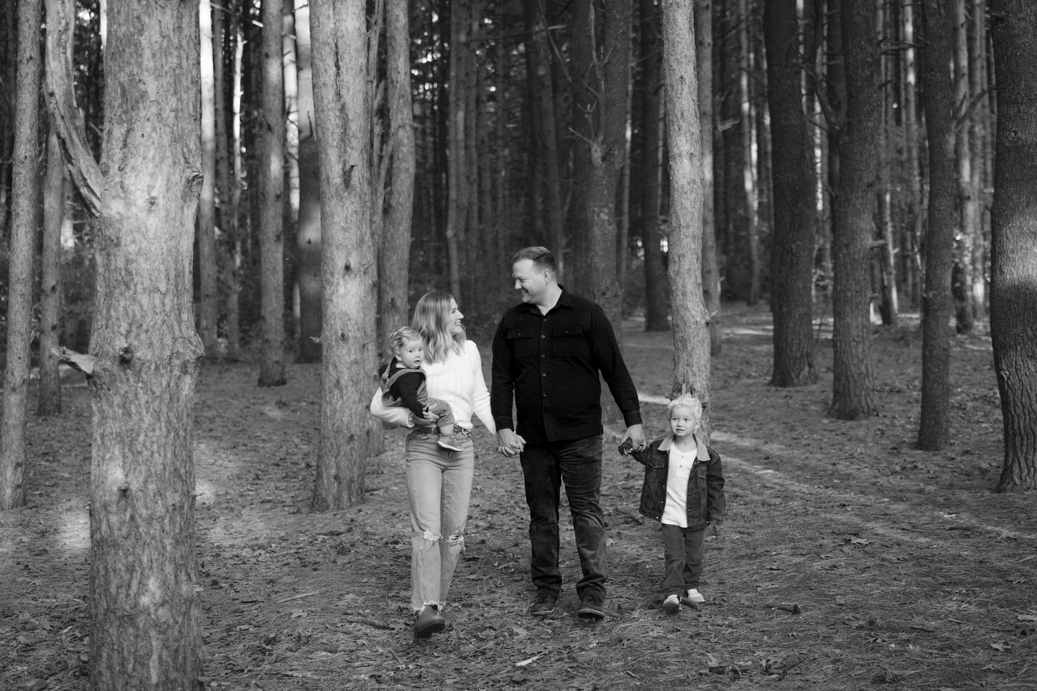 Black and white family portrait taken in a serene forest setting.