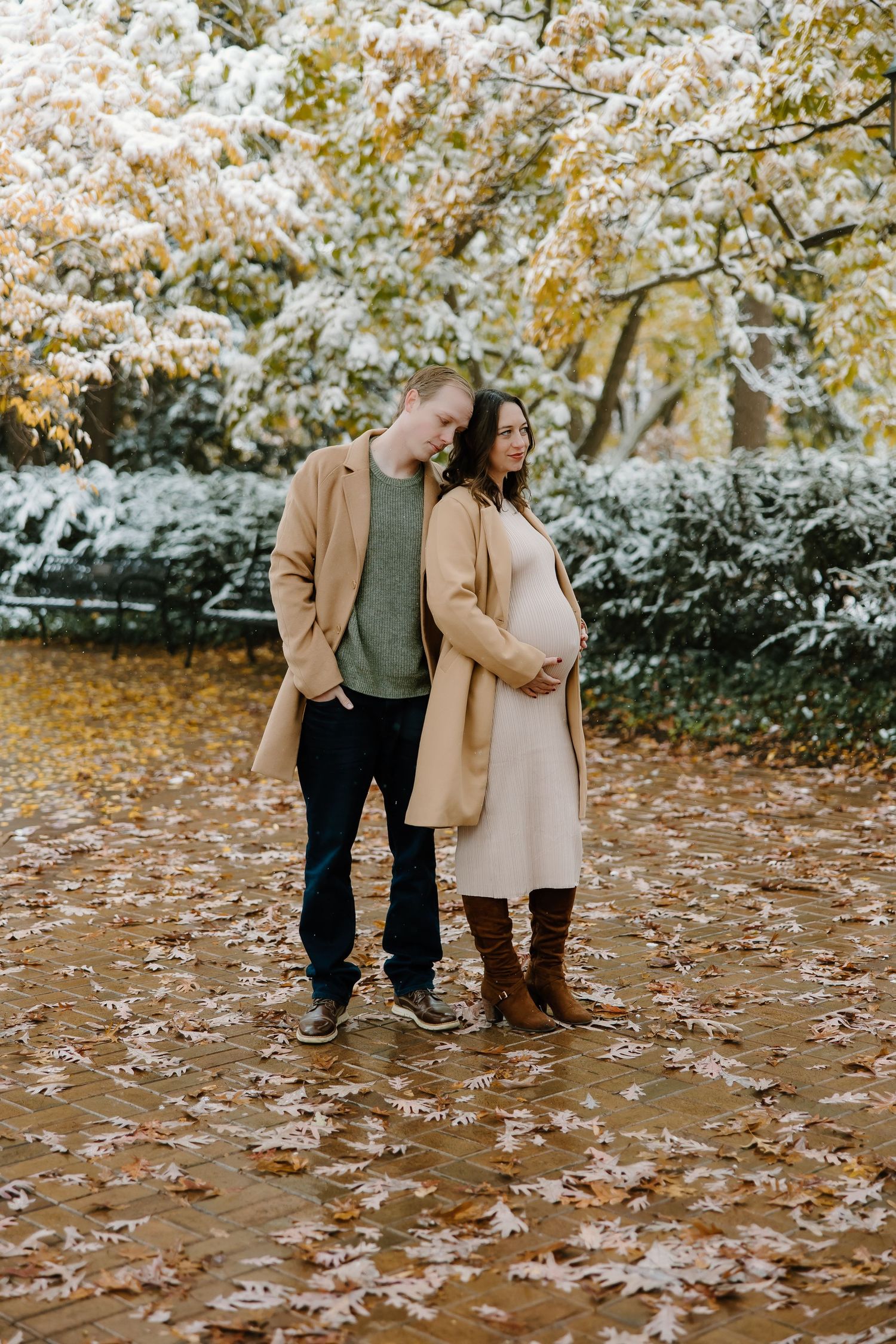 Couple standing on fallen autumn leaves with snow-covered trees in the background.