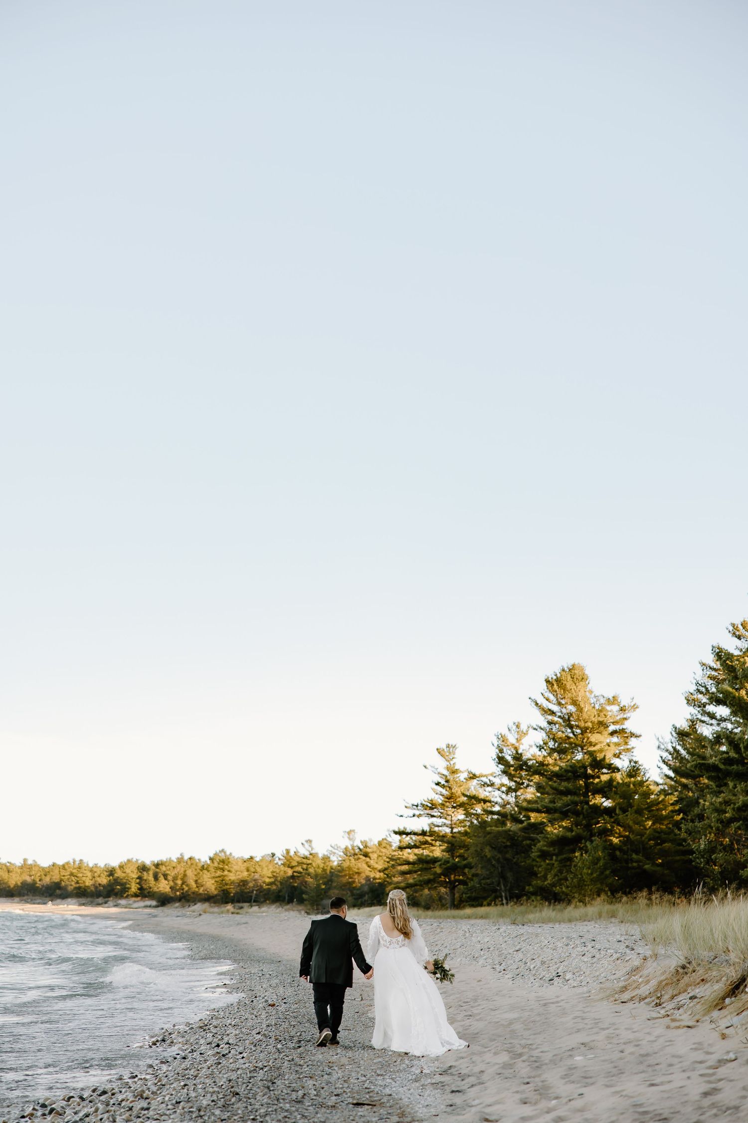 Wedding couple walking along a scenic beach shoreline at sunset.