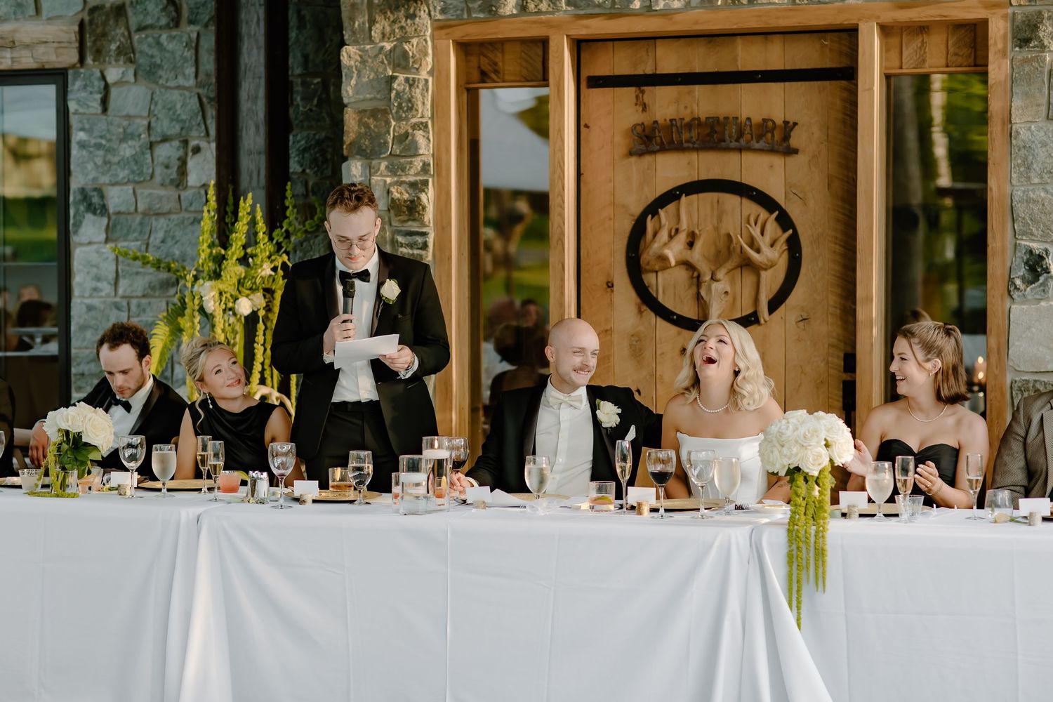 Wedding reception setup in rustic stone venue with wooden details and white tablecloths.