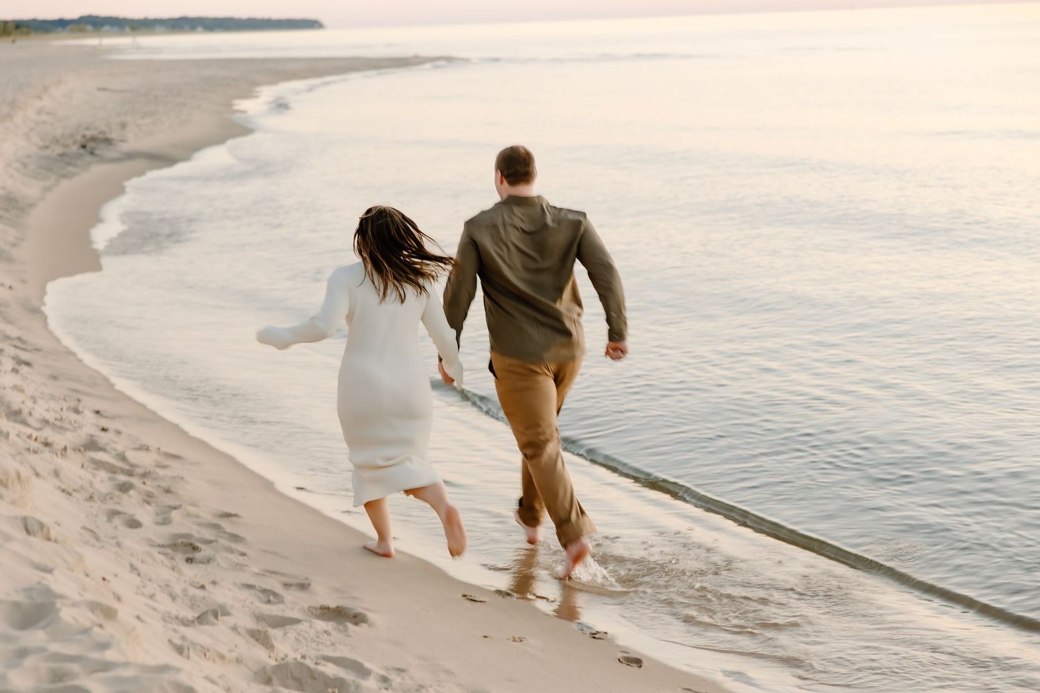 Couple walking along ocean shoreline during sunset with warm tones.