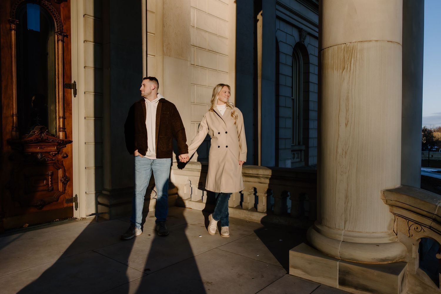 Two people stand in dramatic shadows between classical columns at sunset.