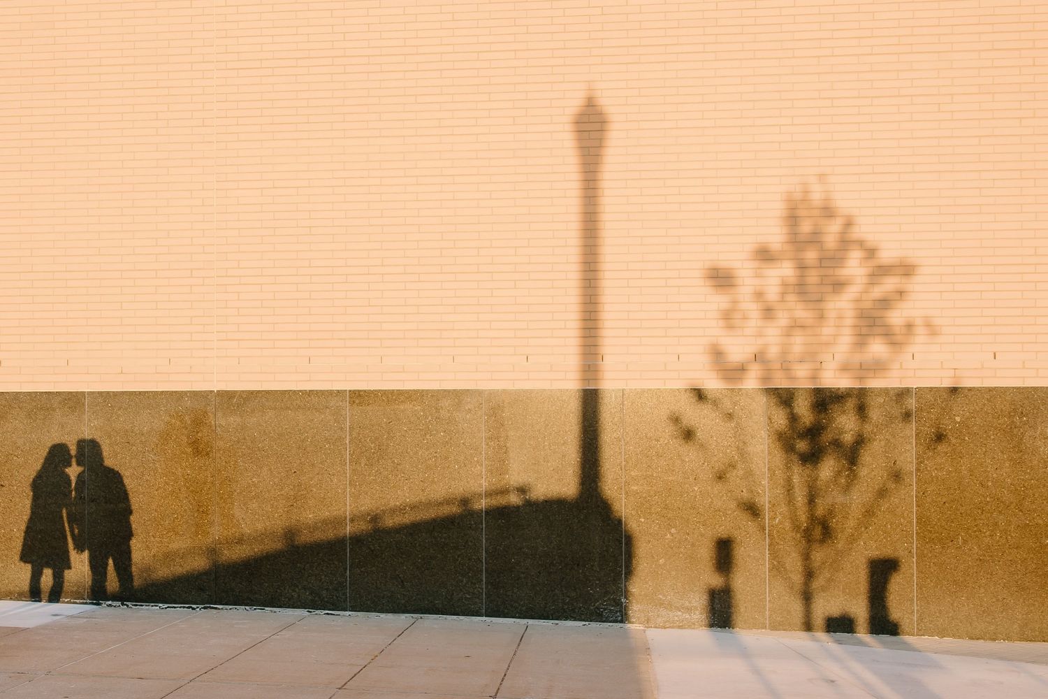 Silhouettes and shadows of couple against warm-toned wall at sunset.